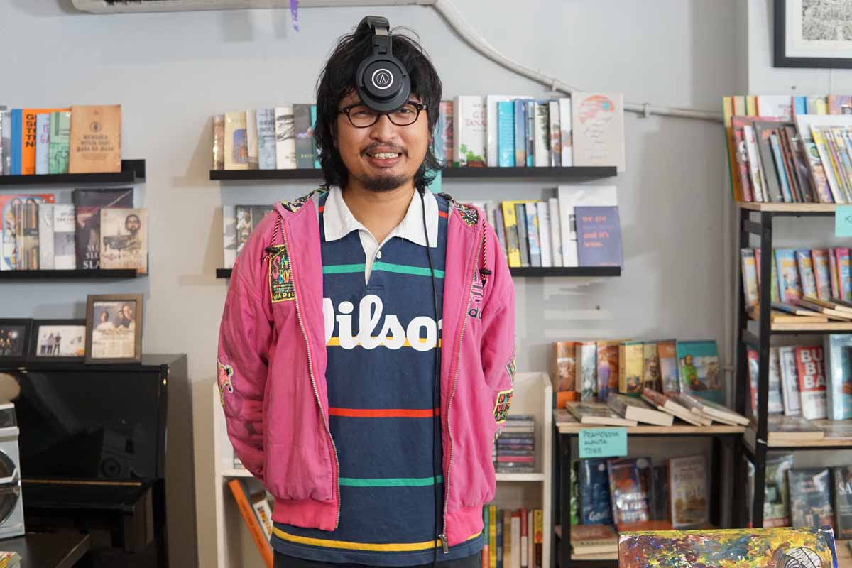 Pemuda Sinarmas dengan polo shirt Wilson dan jaket pink mengenakan headphone di wajahnya